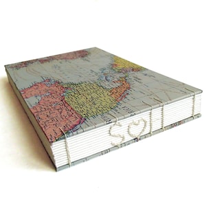 May include: A rectangular hardcover book featuring a vintage world map print on the cover. The book is bound with exposed white stitching along the spine, which forms the letters S and Q in white thread against the white pages of the book block.