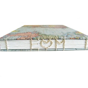 May include: A hardcover book with a vintage world map print on the cover. The spine features exposed coptic stitching in a light beige thread, which is woven to form the letters E, a heart shape, and M across the white paper pages.