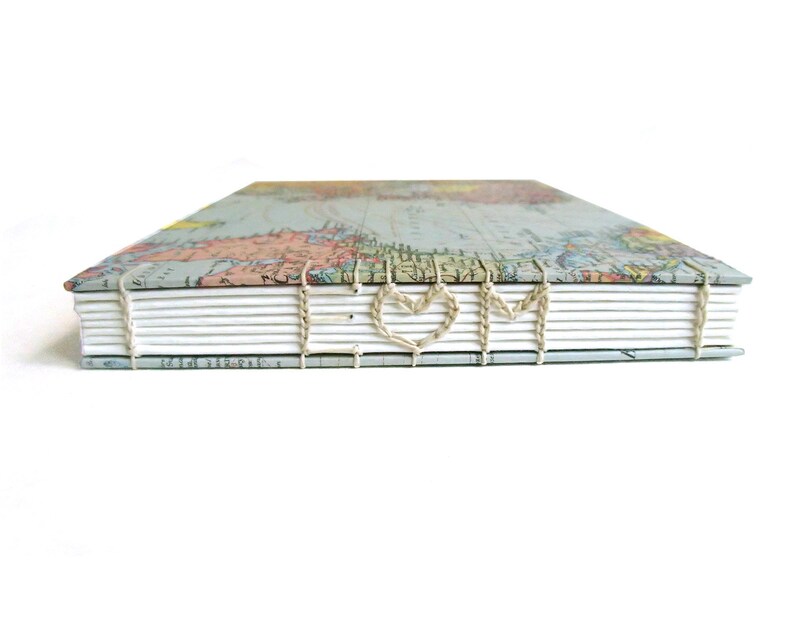 May include: A hardcover book with a vintage world map print on the cover. The spine features exposed coptic stitching in a light beige thread, which is woven to form the letters E, a heart shape, and M across the white paper pages.
