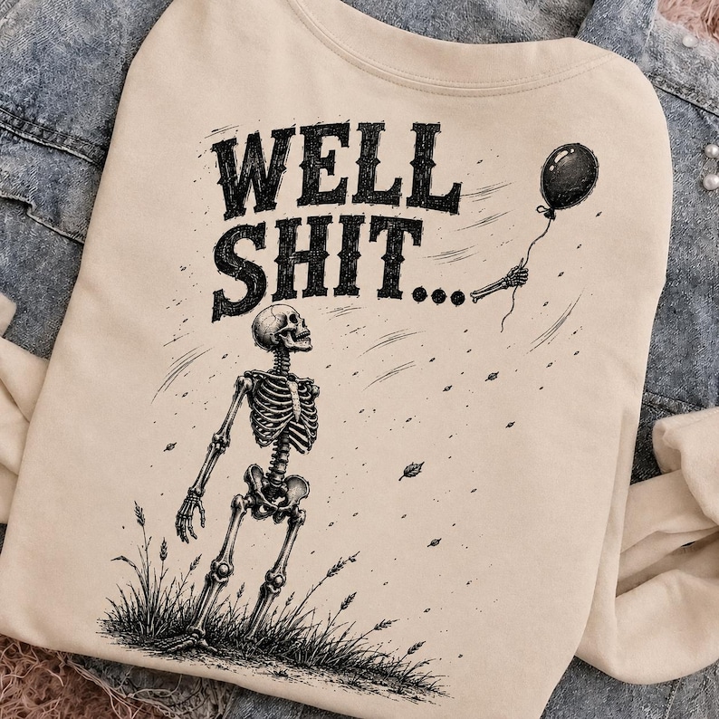 May include: A beige sweatshirt featuring a black graphic illustration of a skeleton standing in a field of grass. The skeleton holds a single black balloon. Above the skeleton, the text reads WELL SHIT... in a bold, distressed black font.
