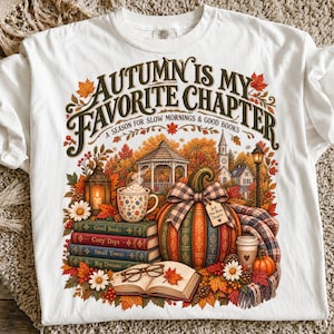 May include: A white t-shirt featuring a graphic with the text "AUTUMN IS MY FAVORITE CHAPTER A SEASON FOR SLOW MORNINGS & GOOD BOOKS". The design includes a stack of books, a pumpkin with a plaid bow, a mug, glasses, and autumn foliage.
