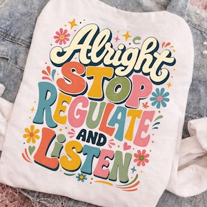Pode incluir: Uma t-shirt branca com uma impressão gráfica multicolorida com o texto Alright STOP REGULATE AND LISTEN. O design inclui várias fontes de estilo retro em tons de laranja, amarelo, rosa, azul e verde, acentuado por pequenos ícones de flores e estrelas.