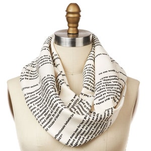 Può includere: Una sciarpa infinita bianca con testo nero stampato su di essa. Il testo è tratto da un libro e include le parole "comportamento affettuoso" e "ha fatto meno per lei".