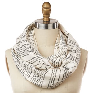 May include: A white infinity scarf with black text from "Alice's Adventures in Wonderland" printed on it. The text includes the quote "What a curious feeling!" and a black and white illustration of the White Rabbit.