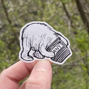 May include: Black and white line art sticker of a bear holding a coffee cup with the word "NY" on it.