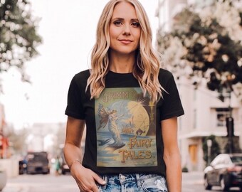 Może przedstawiać: Czarny t-shirt z zabytkową ilustracją z Baśni braci Grimm. Grafika zawiera wróżkę, księżyc i tekst. Koszulka jest noszona przez osobę w niebieskich dżinsach.