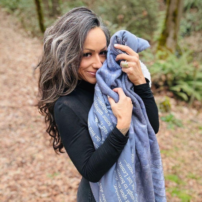 May include: A blue blanket with white text is held up. The blanket has a soft texture and is printed with text from a poem. The person holding the blanket is wearing a black long-sleeved top.