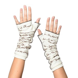 Puede incluir: Un par de guantes sin dedos de color blanco roto con ribete negro y texto de Romeo y Julieta de Shakespeare. Los guantes est&aacute;n hechos de un material suave y tienen un borde con volantes. El texto es de color marr&oacute;n oscuro.