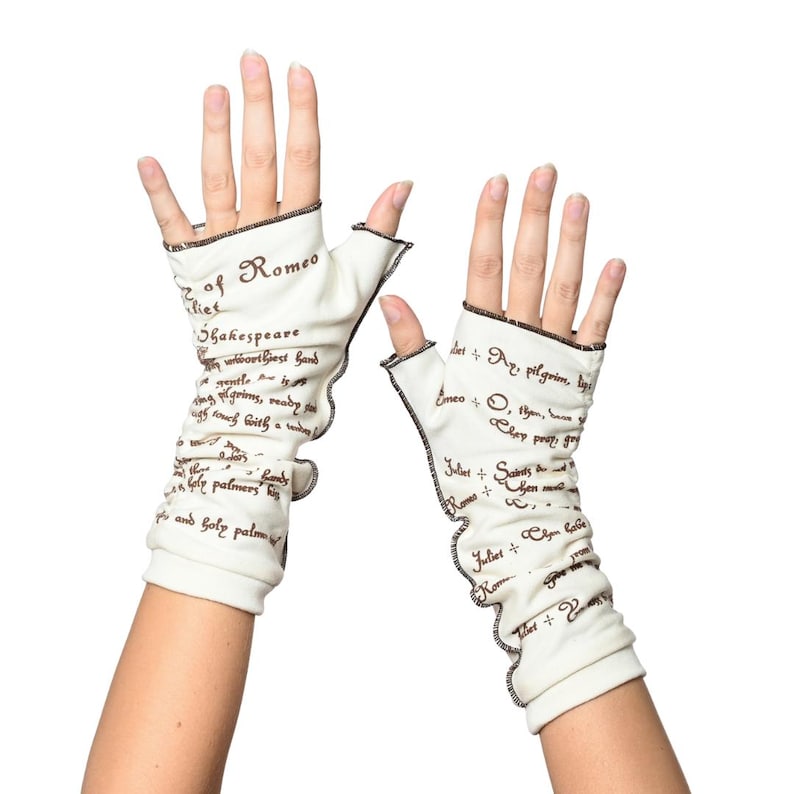 Puede incluir: Un par de guantes sin dedos de color blanco roto con ribete negro y texto de Romeo y Julieta de Shakespeare. Los guantes est&aacute;n hechos de un material suave y tienen un borde con volantes. El texto es de color marr&oacute;n oscuro.