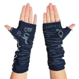 May include: Dark blue fingerless gloves with white stitching and gray text and symbols. The text includes the word "INSTRUMENTS" and various quotes. The gloves are made of a soft material.