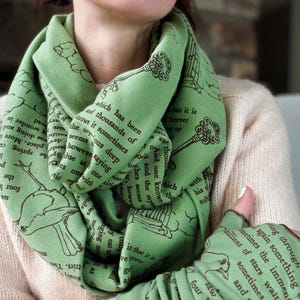 May include: A light green infinity scarf and matching fingerless gloves. The scarf and gloves feature a repeating pattern of keys, birds, and text in a darker green color. The text appears to be from a book.