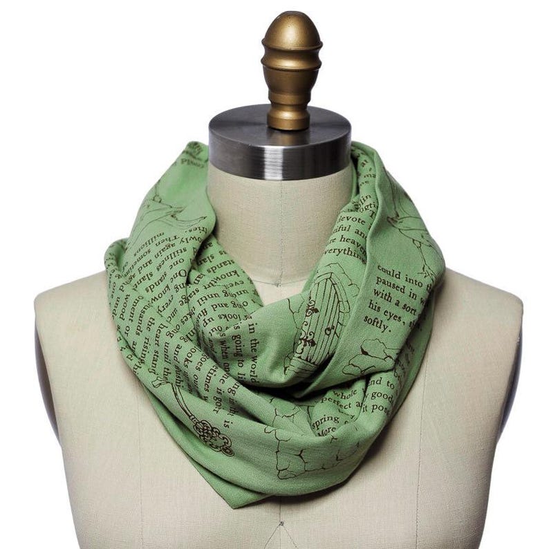 May include: A light green infinity scarf with a printed design featuring text and illustrations. The scarf is draped on a mannequin, showcasing its circular shape and soft fabric. The design includes a key and a door.