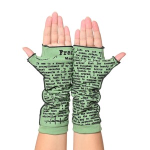 Puede incluir: Un par de guantes sin dedos de color verde claro con costuras negras. Los guantes presentan texto impreso de una novela, con la palabra "Frank" visible. Los guantes est&aacute;n dise&ntilde;ados para cubrir la mano y el antebrazo.