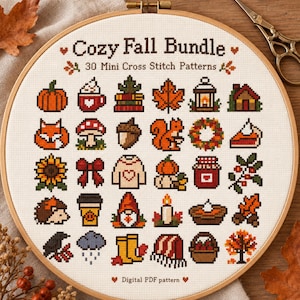 Op de afbeelding: Een houten borduurring met een kruissteekpatroon genaamd Cozy Fall Bundle met 30 herfstachtige mini-iconen, waaronder een pompoen, vos, zonnebloem, egel, koffiebeker, kabouter, kaars, regenwolk en laarzen op een witte stof.