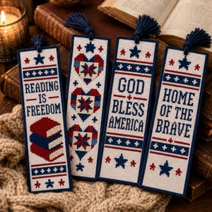 May include: Four rectangular cross-stitch bookmarks with navy blue tassels. The designs feature red, white, and blue patriotic patterns, stars, and text reading Reading Is Freedom, God Bless America, and Home Of The Brave, alongside stacked books.