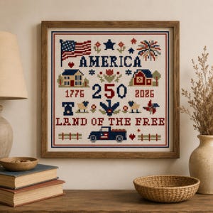 Op de afbeelding: Een ingelijste kruissteek met een patriottisch ontwerp in rood, wit en blauw. Het toont de tekst AMERICA, 1776, 250, 2026 en LAND OF THE FREE. Het patroon bevat een Amerikaanse vlag, een huis, een schuur, een vrachtwagen en bloemmotieven.
