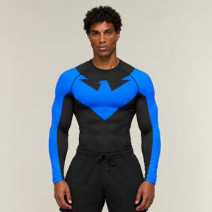 May include: A long-sleeved compression top featuring a black base with vibrant blue panels on the sleeves and a prominent blue bird-shaped emblem across the chest. The garment has a crew neckline and a fitted silhouette, paired with black shorts.
