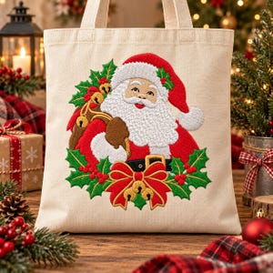 May include: A beige canvas tote bag featuring an embroidered design of Santa Claus wearing a red hat and coat, surrounded by green holly leaves, red berries, and a large red bow with gold bells. The embroidery is centered on the bag.