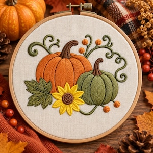 Könnte beinhalten: Ein Stickrahmen mit einem gestickten Motiv aus einem großen orangefarbenen Kürbis und einem kleineren salbeigrünen Kürbis. Das Design umfasst eine leuchtend gelbe Sonnenblume, ein dunkelgrünes Blatt und grüne Ranken mit kleinen orangefarbenen Beeren.