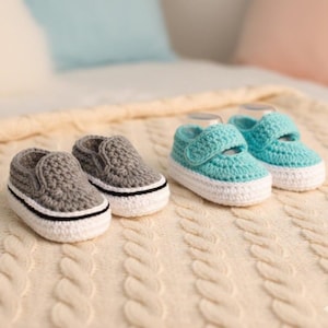 Könnte beinhalten: Zwei Paar handgefertigte Häkelschuhe für Babys. Ein Paar sind graue Slipper mit weißen Sohlen und einem schwarzen Streifen. Das andere Paar ist türkis mit Klettverschluss, weißen Sohlen und einem schwarzen Streifen. Die Schuhe haben eine Textur.