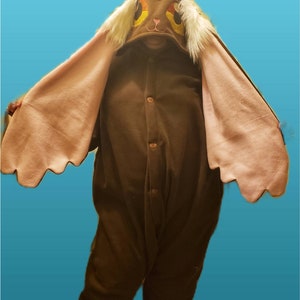 May include: Brown plush jumpsuit with a large hood featuring a cartoon bunny face with pink ears. The hood has a red nose and yellow eyes.