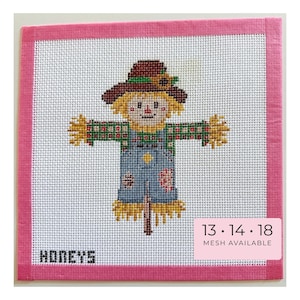 May include: A needlepoint canvas featuring a scarecrow with a brown hat, yellow hair, and blue overalls, framed by a pink border. The text HONEYS appears in the corner, and a pink label states 13, 14, 18 MESH AVAILABLE for this craft project.
