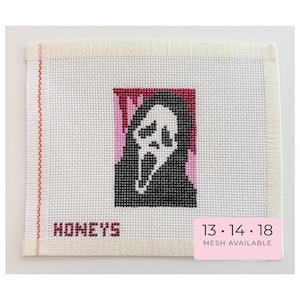 May include: A white needlepoint canvas featuring a cross-stitched design of a black and white ghost-like mask against a pink and red background. The word HONEYS is stitched in red at the bottom left. A pink label reads 13 14 18 MESH AVAILABLE.