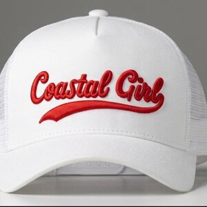 May include: A white trucker hat featuring a structured front panel and a mesh back. The front displays the text Coastal Girl embroidered in a bold red script font with a decorative red underline swoosh extending from the letter l.
