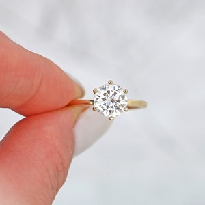 May include: A gold engagement ring with a large, round, clear diamond.