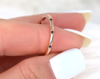 May include: A delicate gold band ring with small black diamonds set in a row around the band.