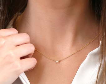 May include: A delicate gold chain necklace with a small, rectangular, clear gemstone pendant.