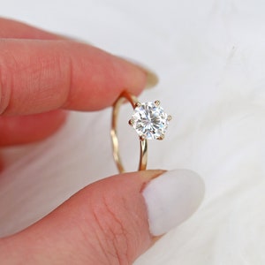 May include: A gold ring with a large, round, clear gemstone set in a six-prong setting.