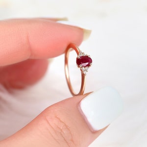 May include: A delicate gold ring featuring a red oval ruby gemstone and small white diamonds on the band.