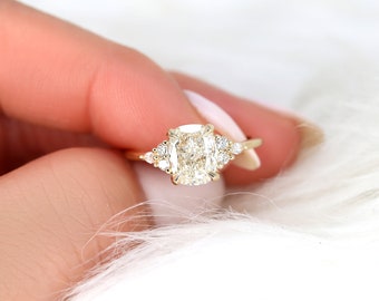 Könnte beinhalten: Ein goldener Verlobungsring mit einem großen, kissenförmigen Diamanten als Mittelstück und kleineren Akzentdiamanten auf der Ringschiene.
