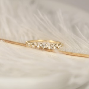 May include: A delicate gold band ring with a row of small, sparkling diamonds set in a zig-zag pattern.