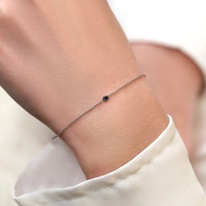 May include: A delicate silver chain bracelet with a single small blue gemstone.