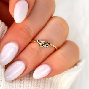 May include: A gold ring with a fan-shaped design. The ring is on a finger with white nail polish.