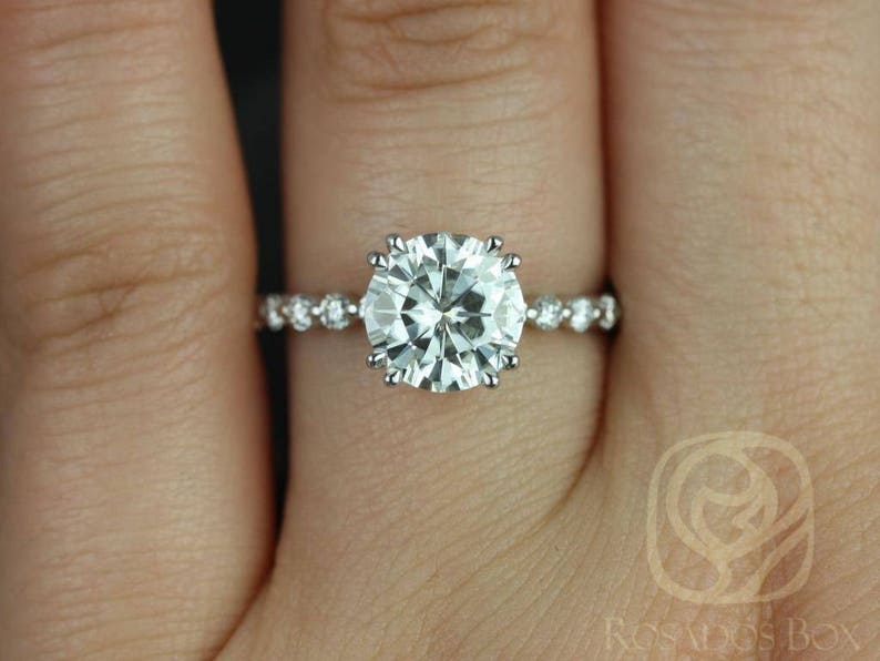 May include: A silver engagement ring with a large, round, clear center stone and smaller, clear stones set in a pave band.