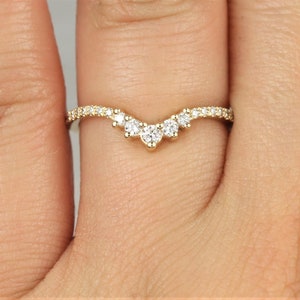 May include: A delicate gold band with a curved row of small diamonds, forming a V-shape.