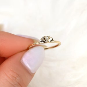 May include: A gold ring with a fan-shaped design on the top. The ring is thin and delicate.