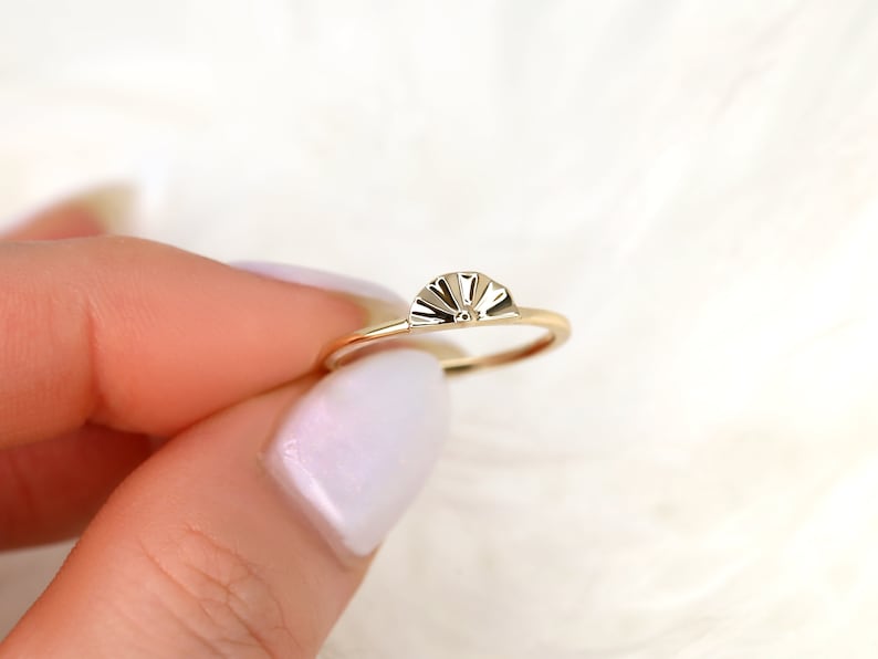 May include: A gold ring with a fan-shaped design on the top. The ring is thin and delicate.