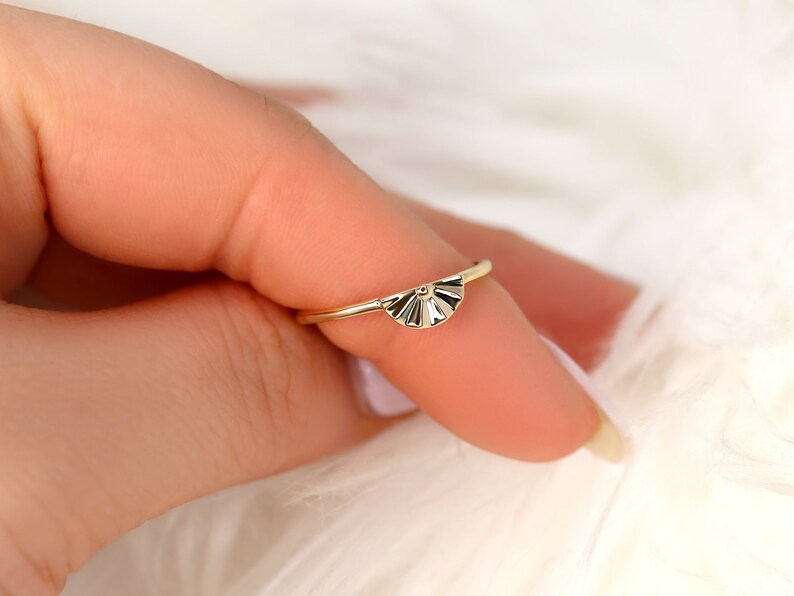 May include: A gold ring featuring a fan-shaped design. The ring is delicate and has a simple, elegant style.