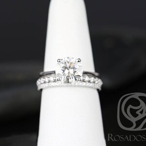 May include: A close-up of a silver engagement ring with a large, round, clear diamond. The ring is on a white display stand.