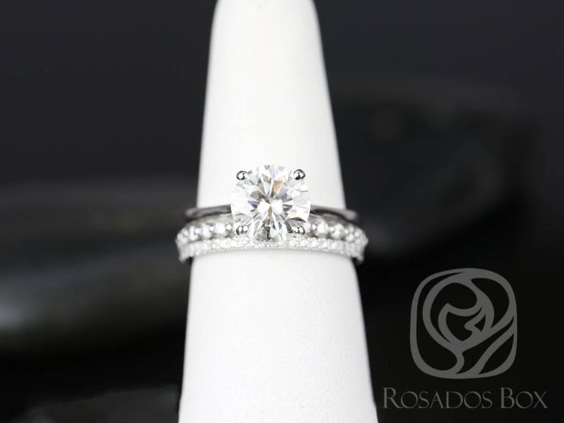 May include: A close-up of a silver engagement ring with a large, round, clear diamond. The ring is on a white display stand.