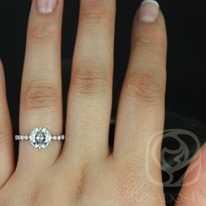 May include: A close-up of a hand wearing a silver ring with a large, round, clear gemstone surrounded by smaller gemstones. The ring is on the ring finger of the left hand.