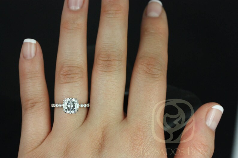 May include: A close-up of a hand wearing a silver ring with a large, round, clear gemstone surrounded by smaller gemstones. The ring is on the ring finger of the left hand.