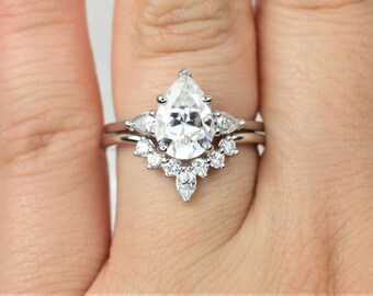 May include: A pear-shaped diamond engagement ring with a halo of smaller diamonds. The ring is set in a white gold band.