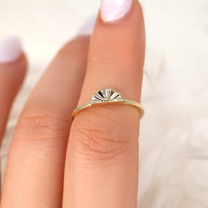 May include: A gold ring featuring a sun-shaped design. The ring is worn on a finger.