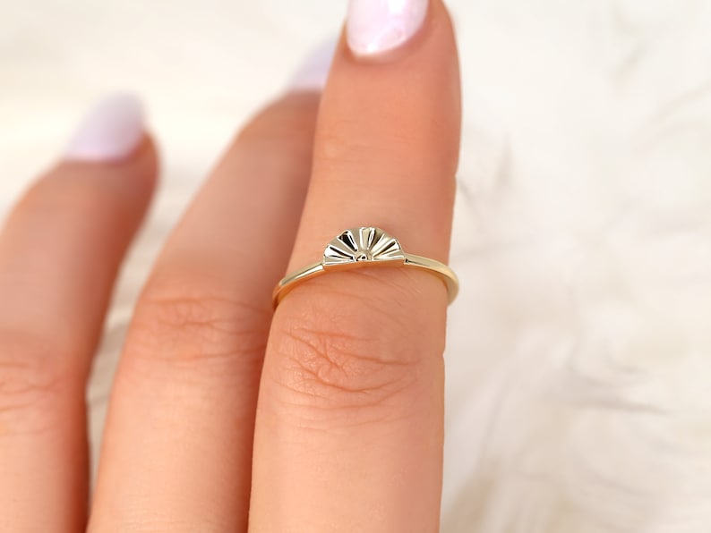 May include: A gold ring featuring a sun-shaped design. The ring is worn on a finger.