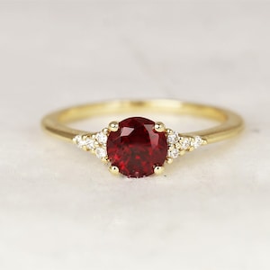 May include: A gold ring featuring a large, oval ruby gemstone surrounded by smaller diamonds. The ring has a plain band.